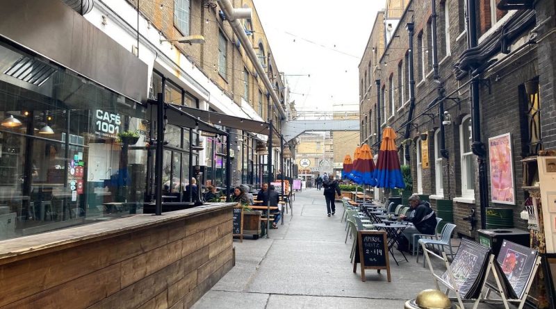 View down Dray Walk, Brick Lane, with outdoor seating and umbrellas.