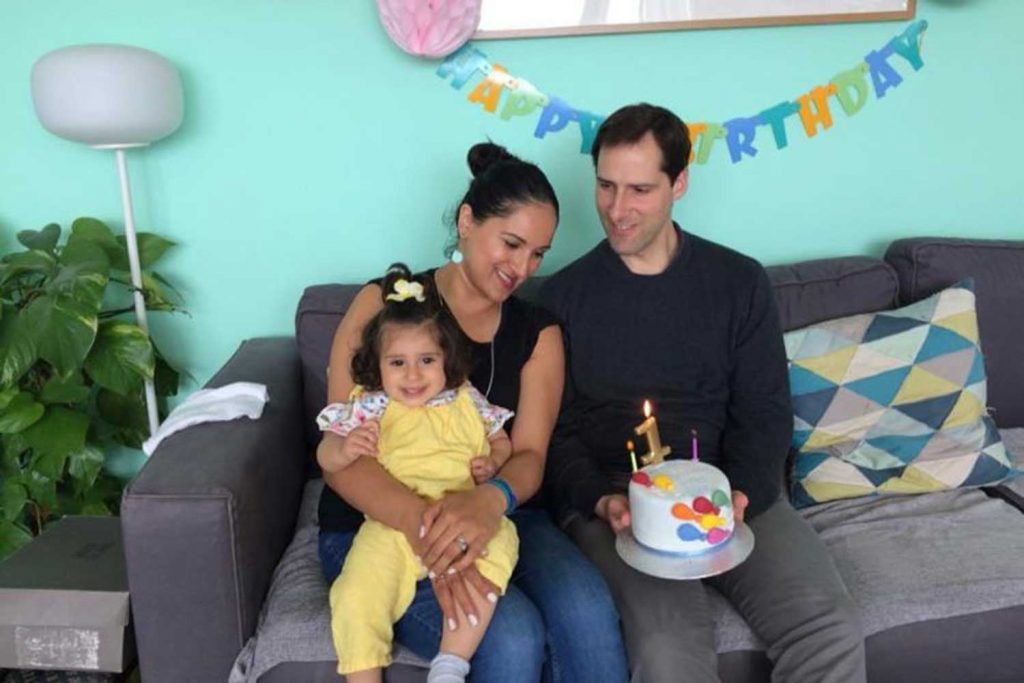 Faryal and Juan Iqbal and their daughter, Inaya, sitting on a sofa with a cake to celebrate Inaya's first birthday. 