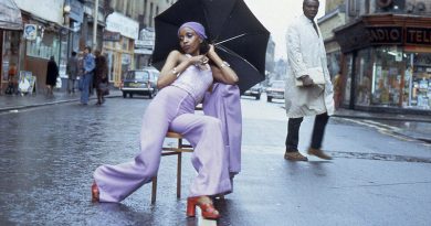 Armet Francis fashion photograph of woman on chair posing in a purple jumpsuit holding a black umbrella.