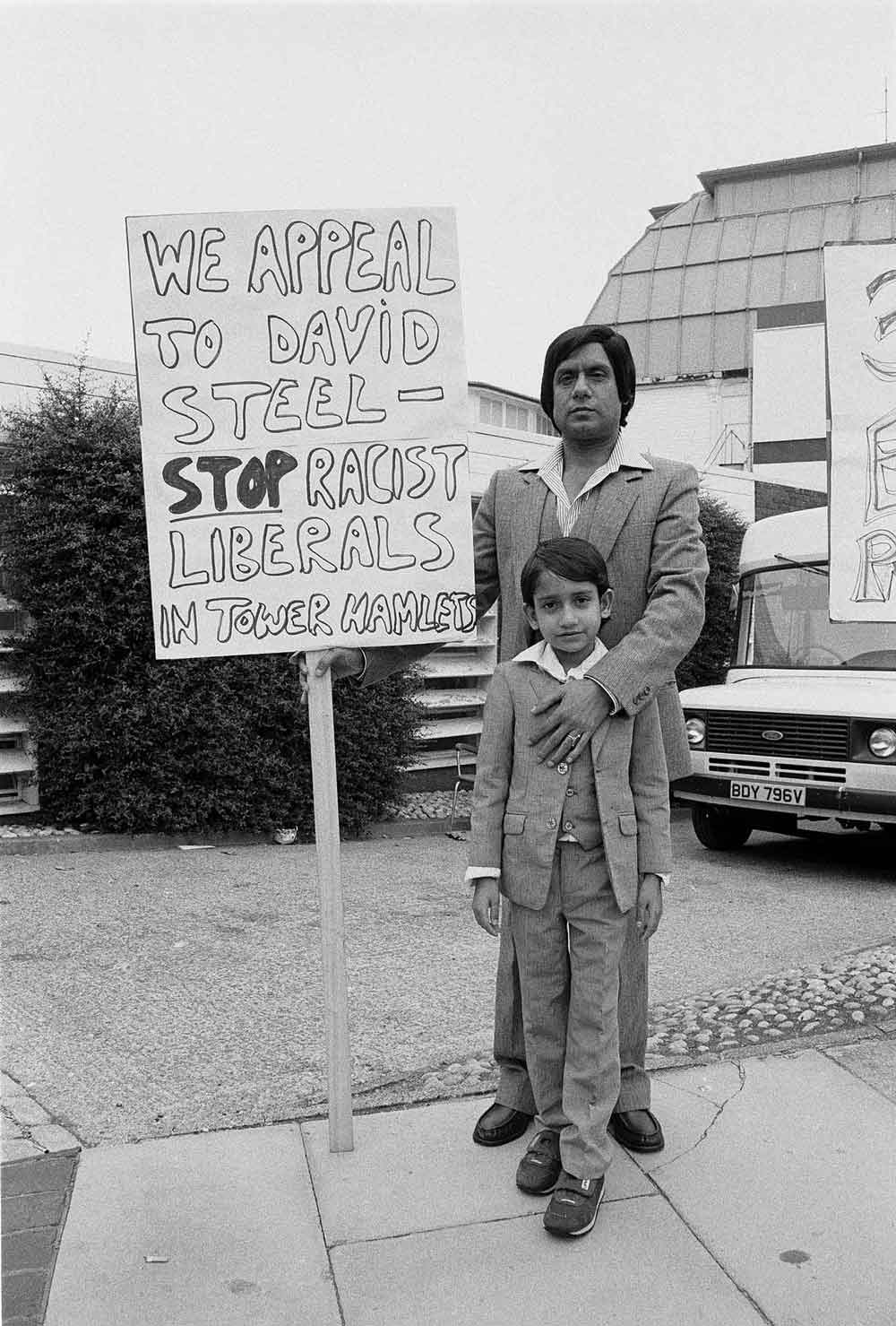 Suited Bengali father and son protesting against Liberal Democrat policy in Tower Hamlets in the 1990s: Images of Housing, Homelessness and Resistance in London's East End, from the Conditions of Living exhibition at Four Corners.