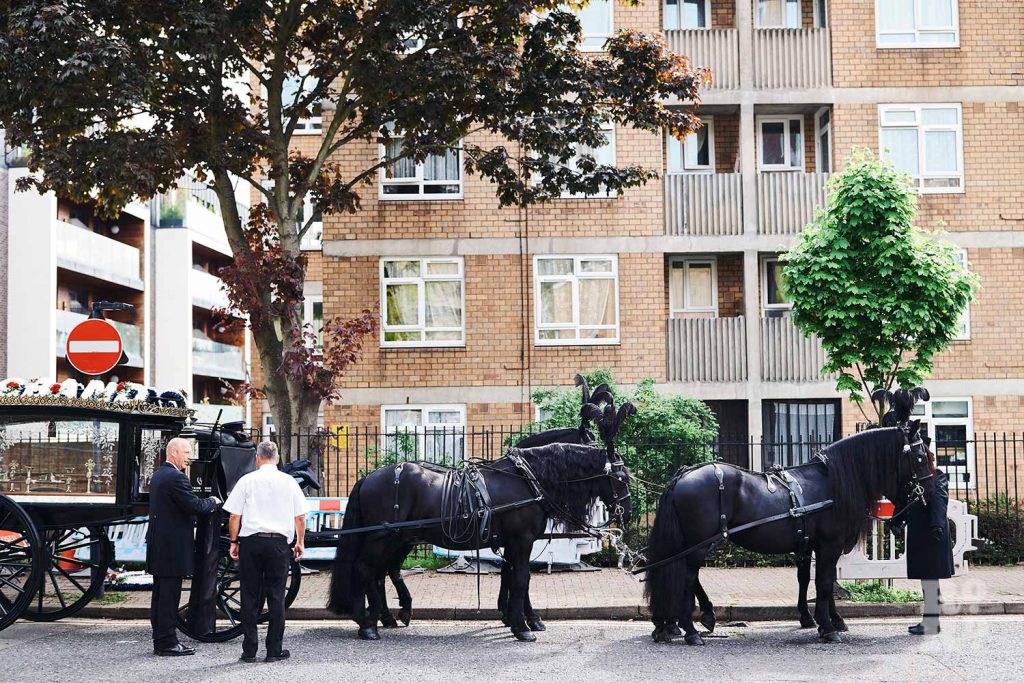 Four black Friesian horses leading a horse-drawn carriage in a funeral in the East End.
