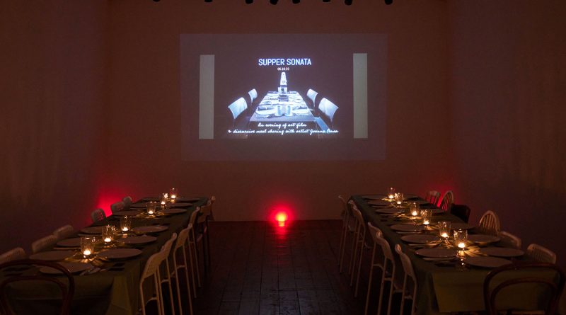Candle-lit dining tables and projector set up for a supper club and film screening in the Nunnery Gallery.