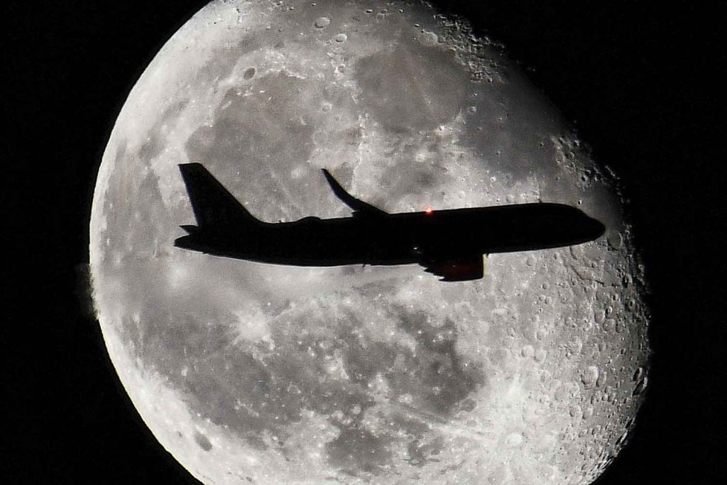 Plane on approach into London Heathrow Airport passing in front of the moon © Phil Verney