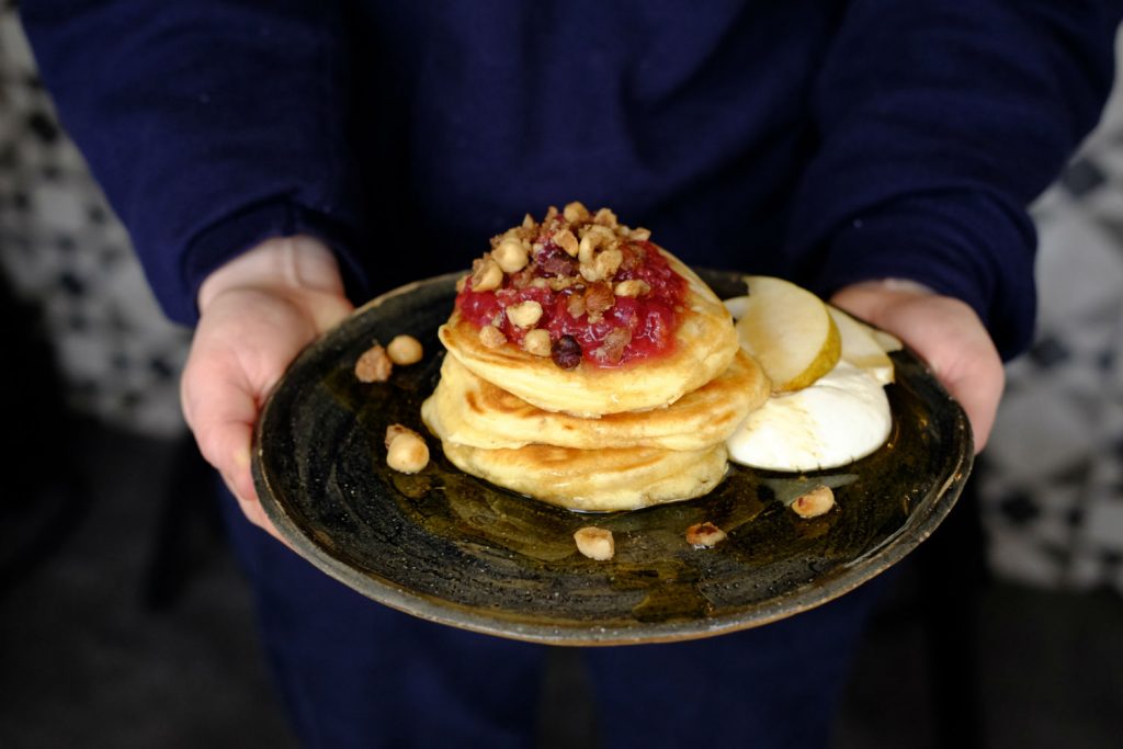 Fluffy American style pancakes topped with fruit and nuts on a dark plate served at Mae and Harvey on Roman Road, Bow, East London