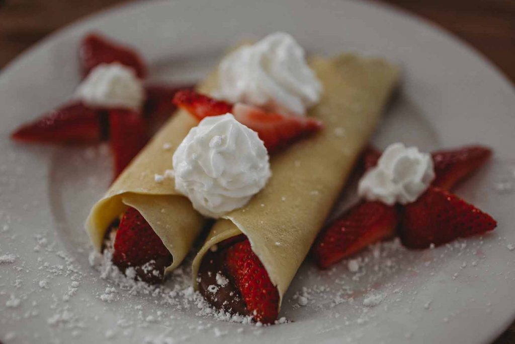 Pancakes filled with strawberries and topped with whipped cream on a white plate, served at Sweet Talkers, Roman Road, Bow, East London