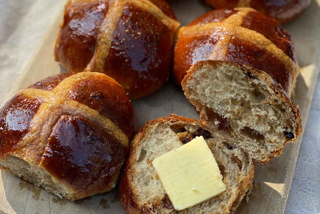 Four hot cross buns and butter on a chopping board from E5 Bakehouse in Hackney