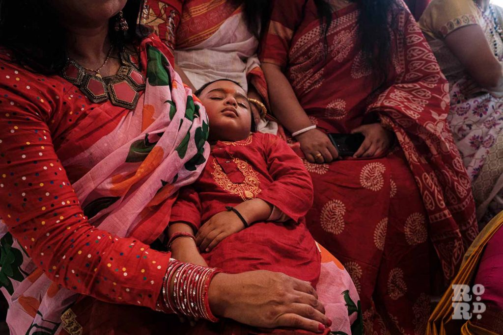 A baby fast asleep in mothers arms, at Holi festival, or Dolyatra, at the Hindu Pragati Sangha in Mile End, East London.