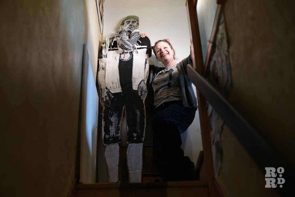Artist Sylvia Difino standing on her staircase with a life-size sculpture of a man in a scarf