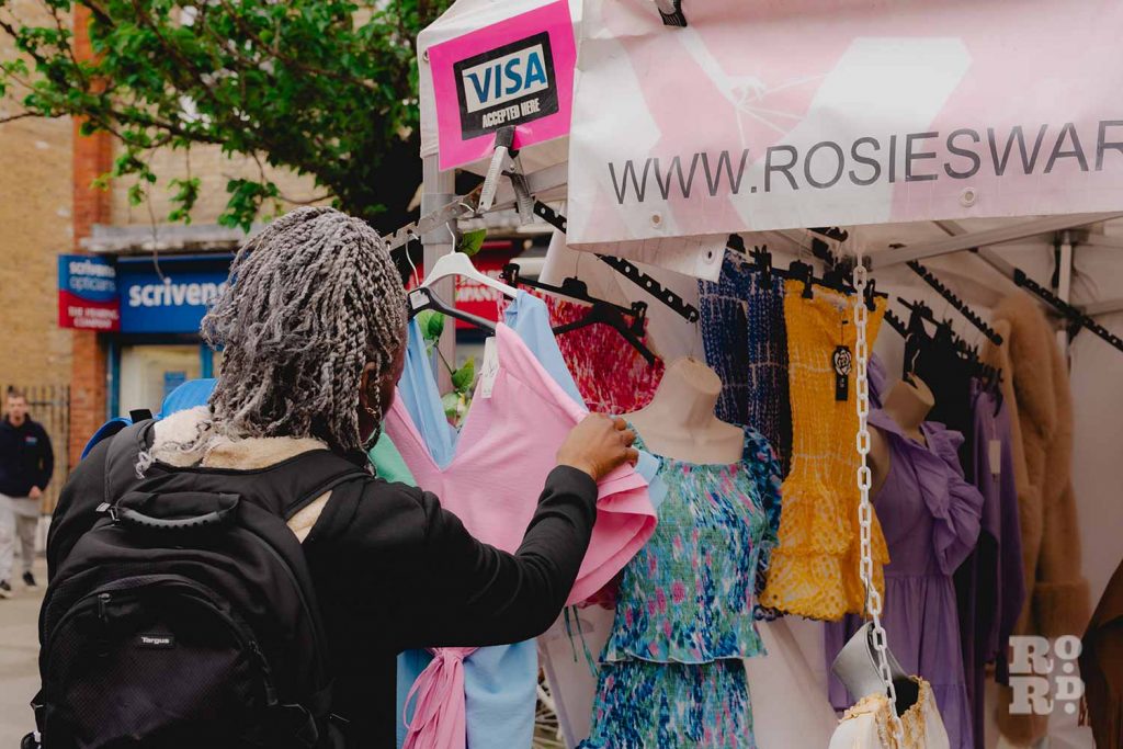 A customer browsing a pink blouse at Rosie Smyth's ladies' fashion stall on Roman Road Market.