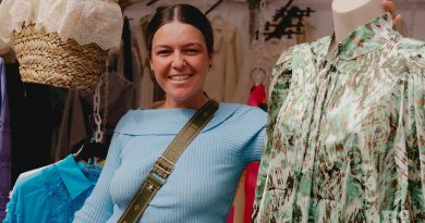 Rosie Smyth, a Roman Road Market trader, at her ladies fashion stall, leading against a mannequin displaying a green, patterned dress.