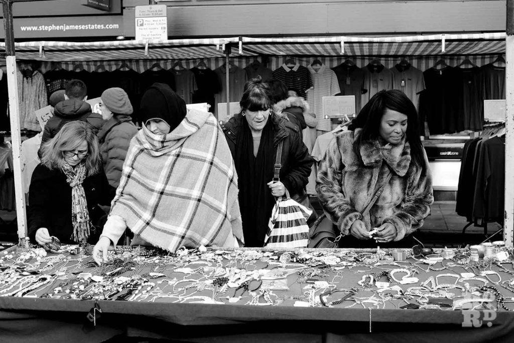 A stall selling jewellery with Asian and Black Afro-Caribbean women shoppers on Roman Road Market, Bow, East London.
