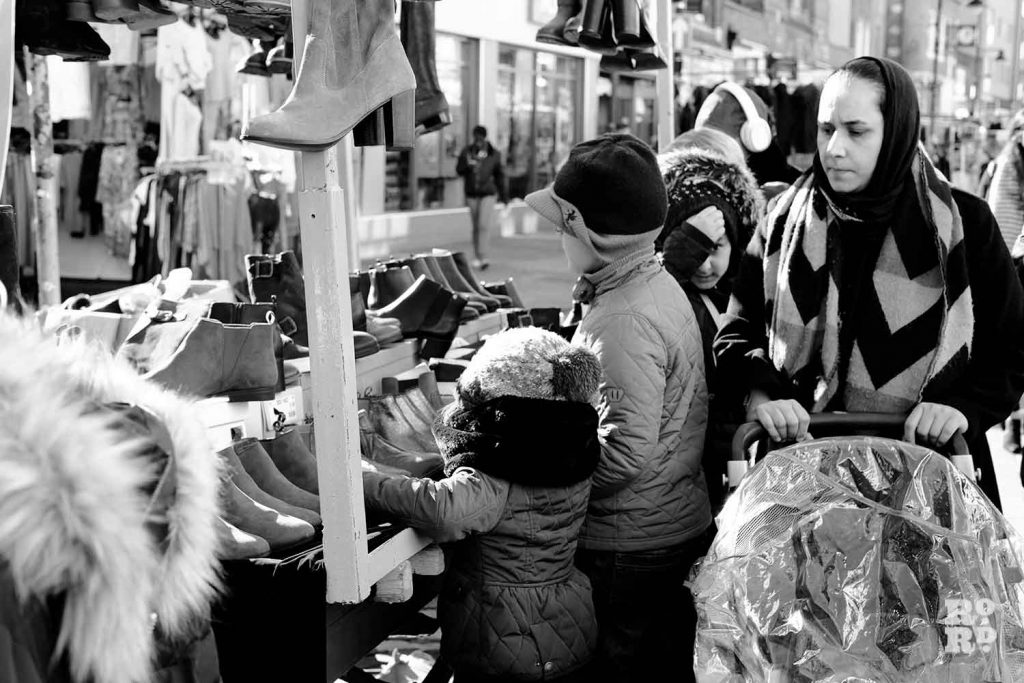 Mother with her children looking at shoes and boots on Roman Road Market, Bow, East London.