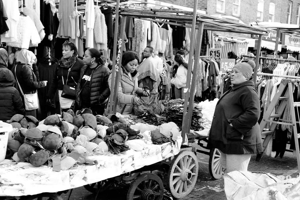 Afro-Caribbean woman trader selling women's underwear on Roman Road Market, East London.