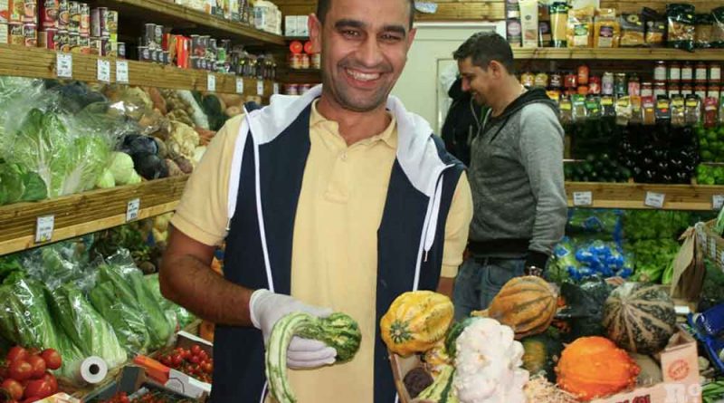 A shopkeeper holding box of pumpkins and squashes in a fruit and veg shop on Roman Road, Bow, East London.