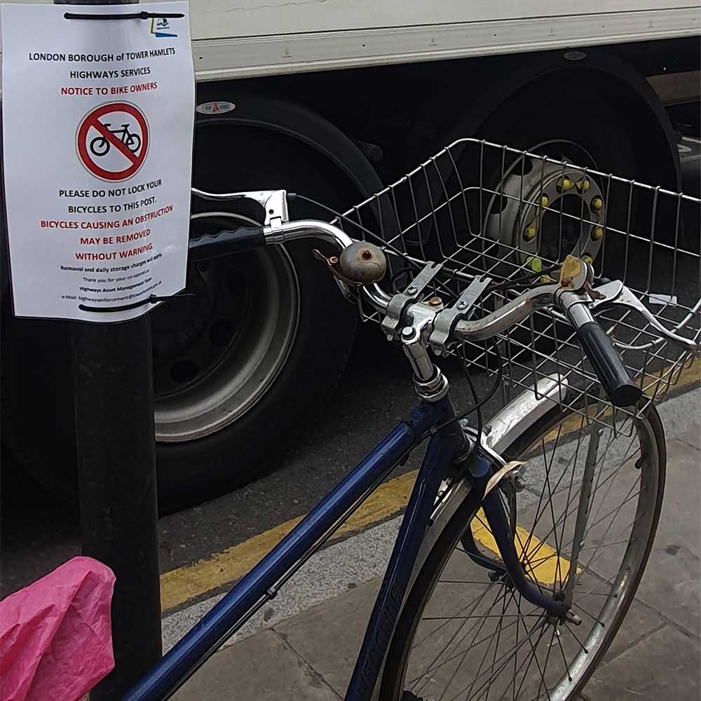 A removal sign posted next to a bike locked to a pole, Roman Road, East London