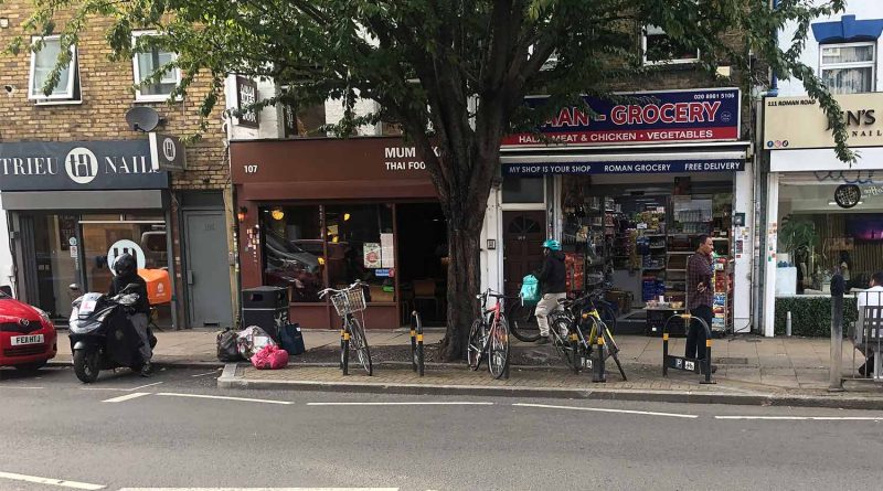 Bicycles locked on the other side of the road by a tree and some shops, Roman Road, East London