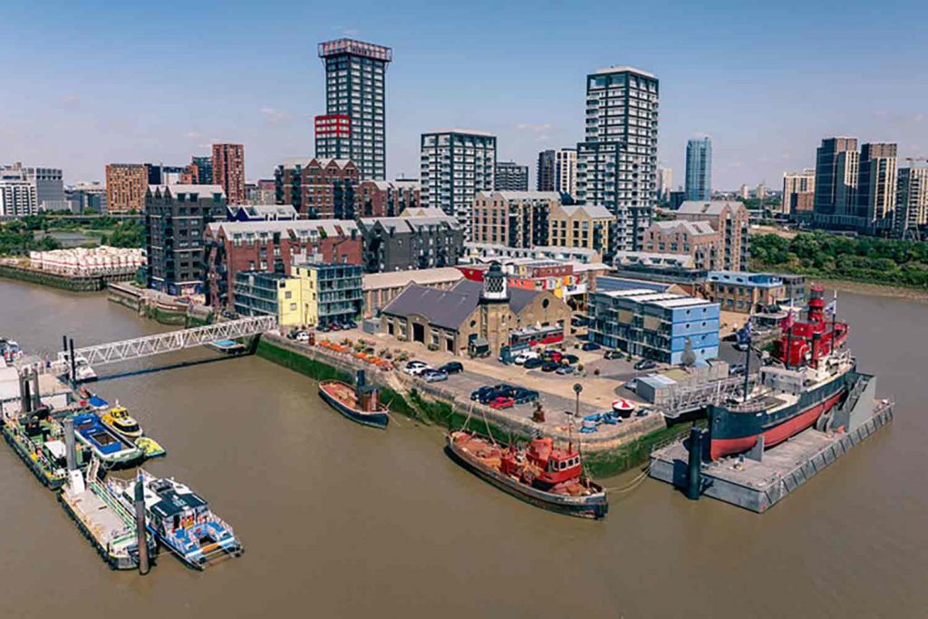An aerial shot of Trinity Buoy Wharf and Container City surrounded by the Thames with high rises in the background, Poplar, east London